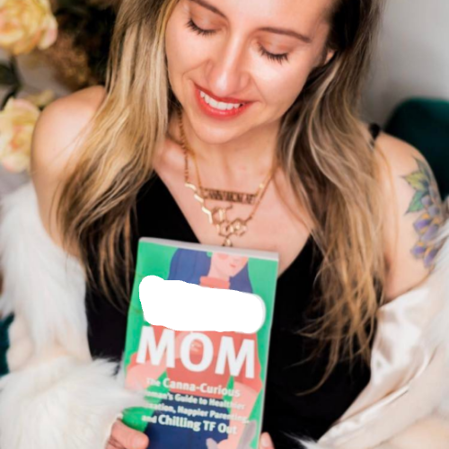 Woman holding a book titled 'Canna-cruious Mom guide book' with a blurred background